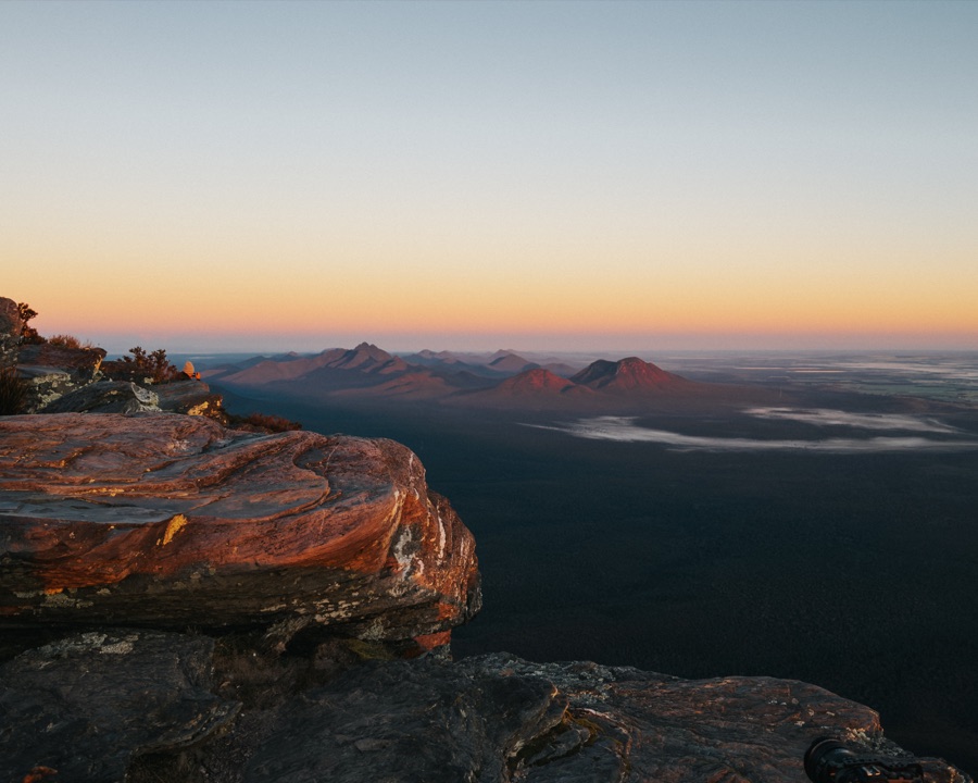 Warm sunrise light across a rocky Bluff Knoll summit and distant ranges